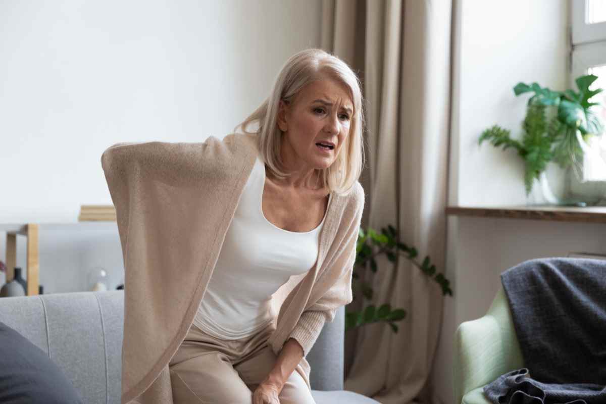 Reife Frau mittleren Alters fühlt sich verletzt, plötzliche Rückenschmerzen berühren die schmerzende Wirbelsäule allein zu Hause.