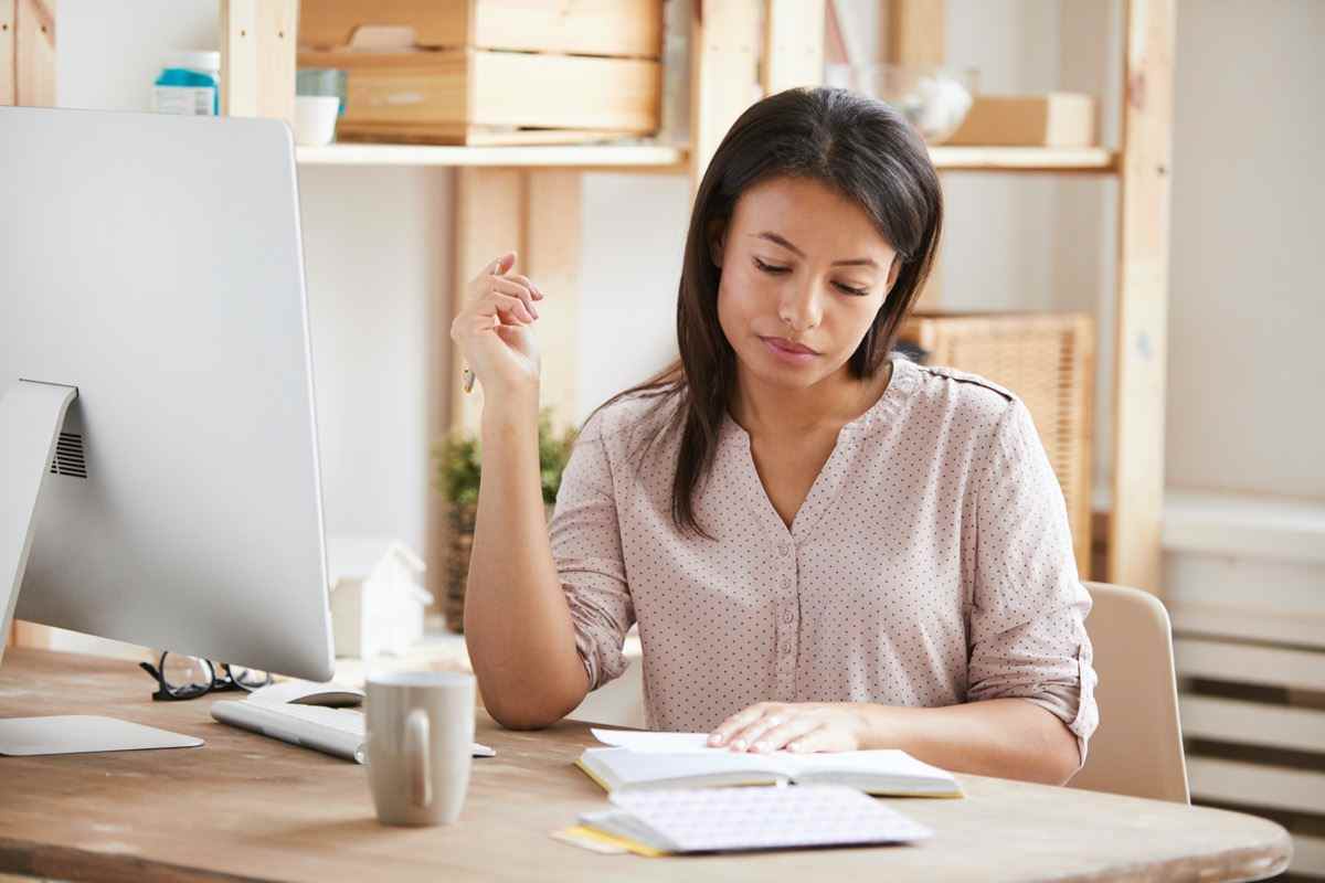 Porträt einer schönen Frau mit gemischter Abstammung, die im Notizbuch schreibt, während sie am Schreibtisch im Büro sitzt, Platz kopieren