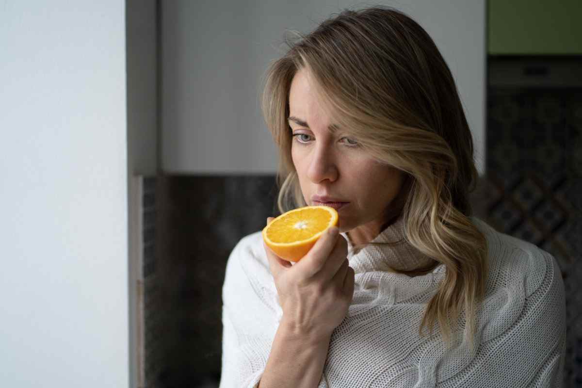 Frau, die versucht, den Geruch von halb frischer Orange zu riechen, hat Symptome von Covid-19