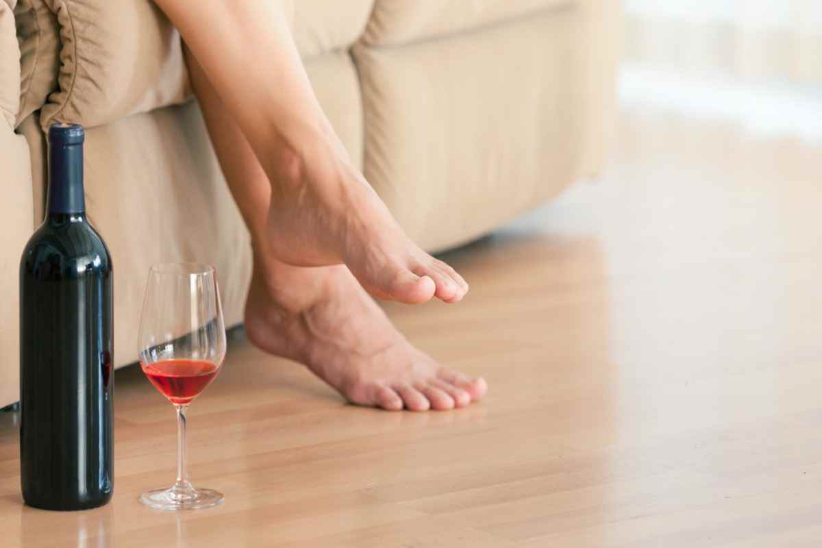 Frau entspannt sich zu Hause auf dem Sofa mit einer Flasche Wein und einem Glas an ihrer Seite.