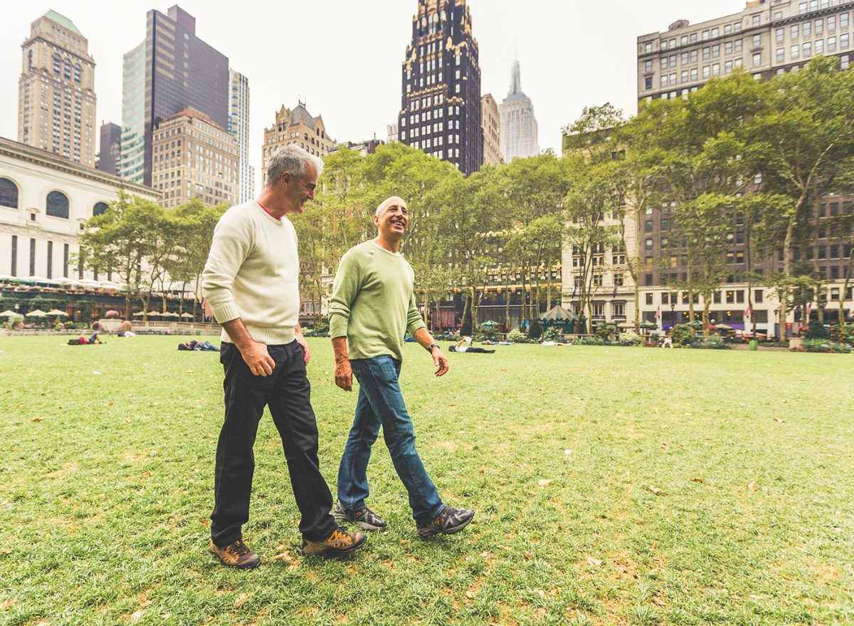 Zwei Männer gehen zusammen in einem Stadtpark mit Gebäuden hinter sich