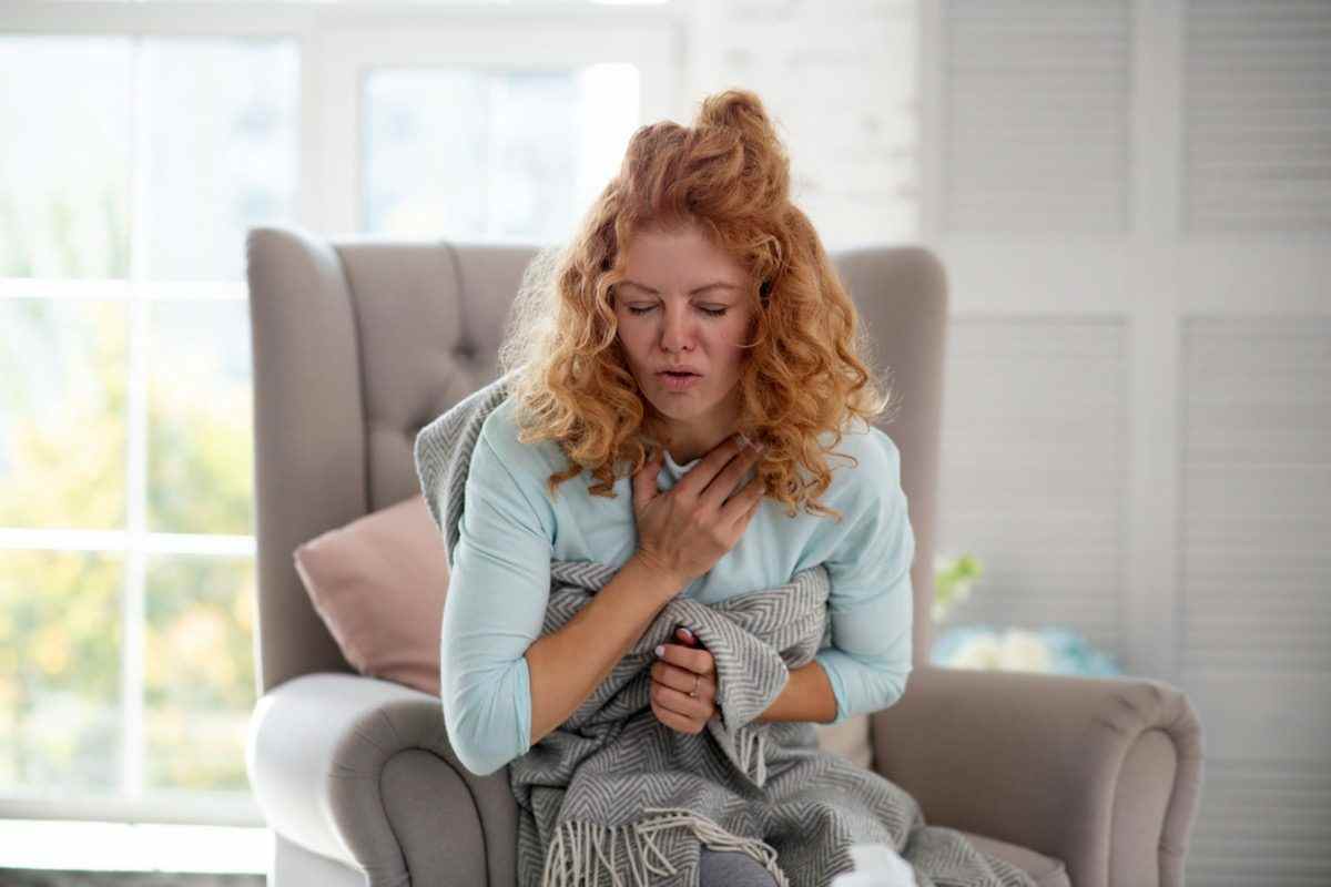 Lockige Frau, die sich schlecht fühlt und unter starkem Husten leidet, während sie Grippe hat