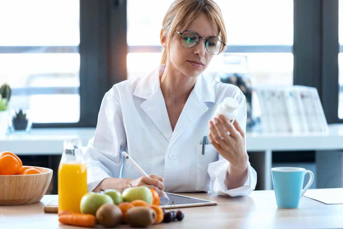 Aufnahme von Ernährungsberaterin Arzt schreibt das ärztliche Rezept für eine richtige Ernährung auf einem Schreibtisch mit Früchten, Pillen und Nahrungsergänzungsmitteln.