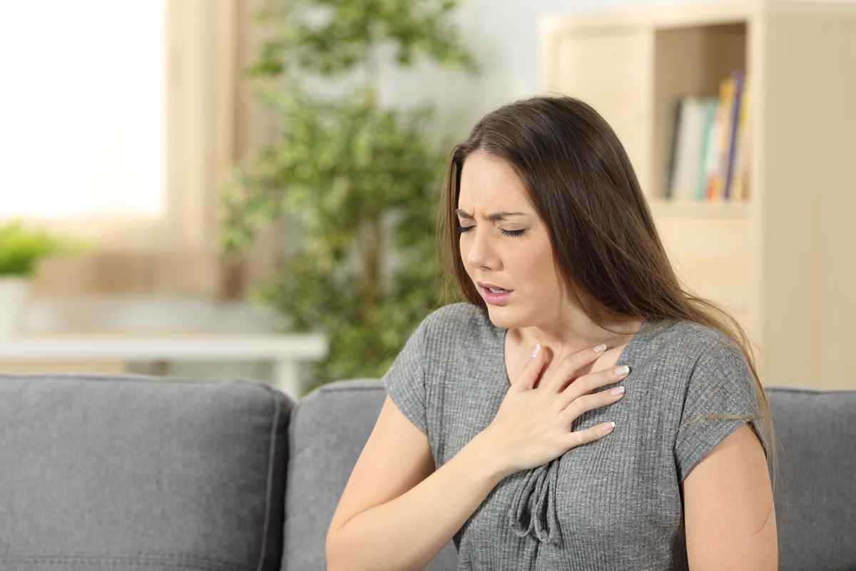 Frau mit Atemproblemen, die zu Hause auf einer Couch im Wohnzimmer sitzt