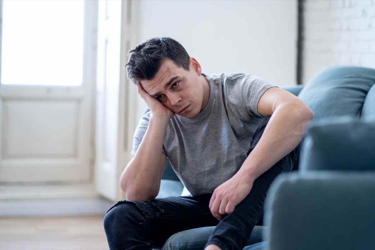 Porträt eines jungen Mannes, der depressiv und verzweifelt weinte, allein im Sofahaus, der unter emotionalen Schmerzen und Unglück leidet