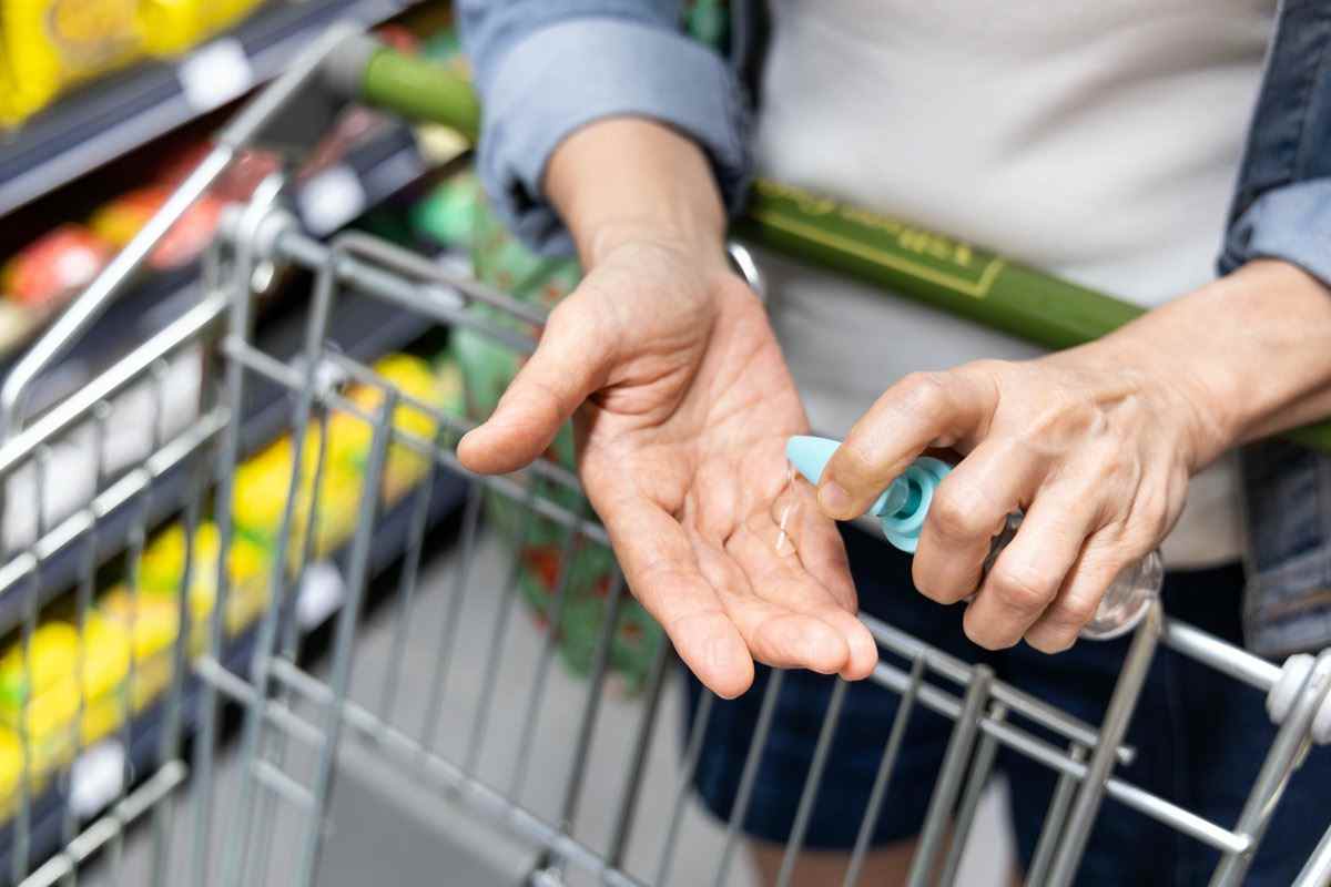 Asiatische Käufer desinfizieren die Hände mit Desinfektionsmittel im Supermarkt beim Einkaufen von Lebensmitteln.  Der öffentliche Einkaufswagen ist eine Kontaktstelle für Viren und Bakterien mit hohem Risiko.