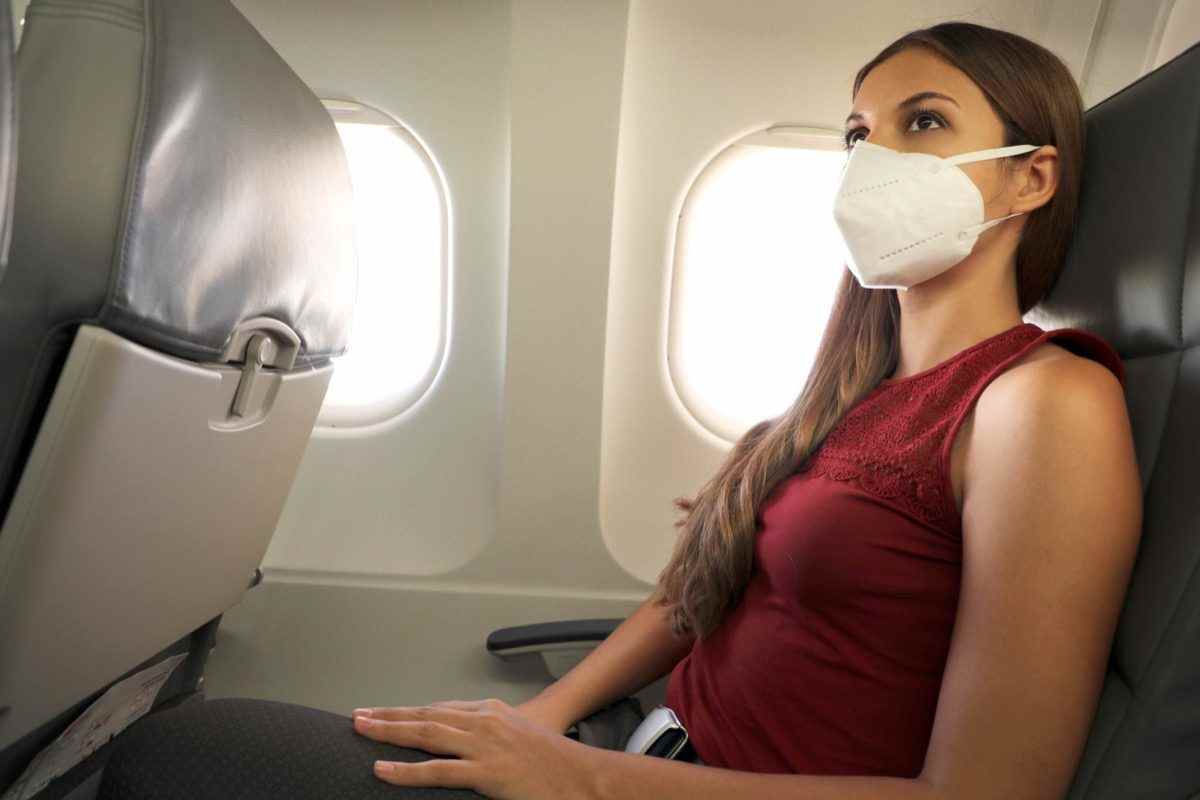 Frau sitzt im Flugzeug und trägt eine KN95 FFP2-Schutzmaske