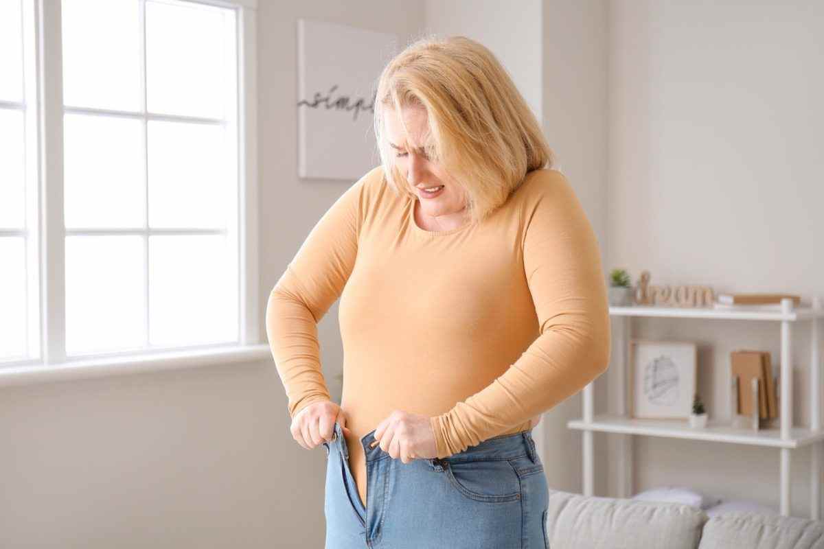 Übergewichtige Frau in engen Kleidern zu Hause versucht, in enge Jeans zu passen.