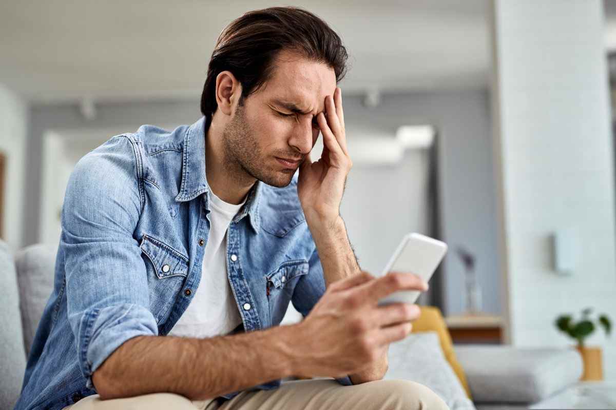 Mann benutzt Smartphone und hält sich zu Hause den Kopf vor Schmerzen