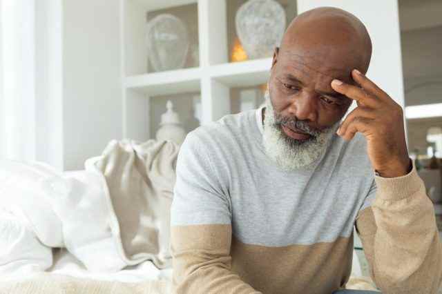 Älterer afroamerikanischer Mann, der auf weißem Sofa im hellen Raum im Strandhaus sitzt?