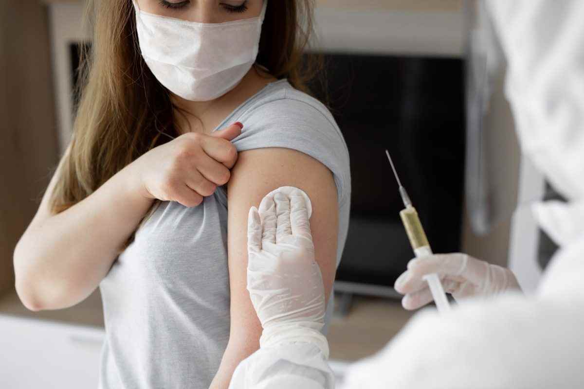 Arzt in persönlichem Schutzanzug oder PSA injiziert Impfstoff, um die Immunität einer Patientin zu stimulieren, bei der das Risiko einer Coronavirus-Infektion besteht.