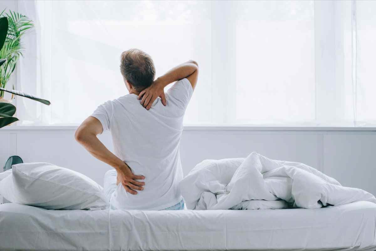 Rückansicht eines Mannes, der auf dem Bett sitzt und an Rückenschmerzen leidet