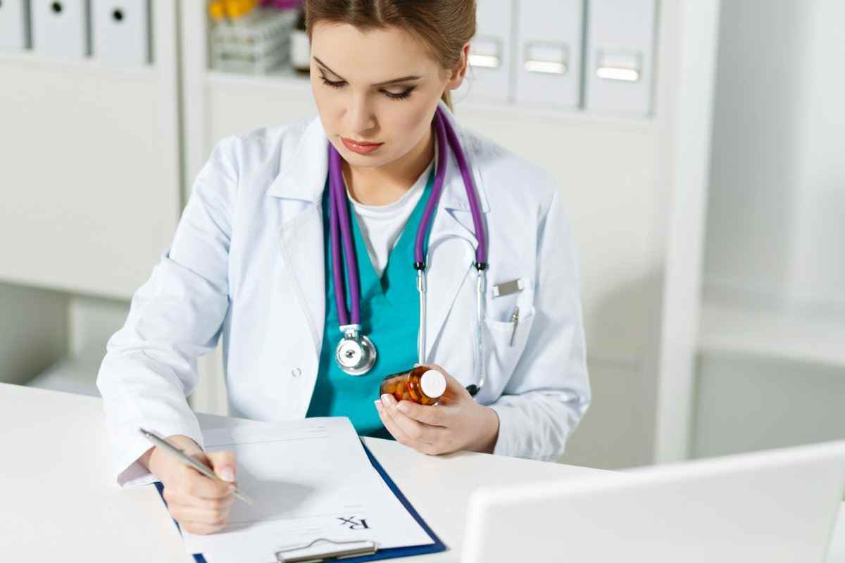 Arzt Medizin Arzt oder Apotheker sitzt am Arbeitstisch, hält ein Glas Pillen in den Händen und schreibt Rezepte auf speziellem Formular.