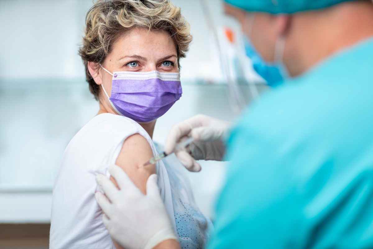 Patientin, die hinter der Gesichtsmaske und mit den Augen lächelt, während sie eine Grippeimpfung bekommt