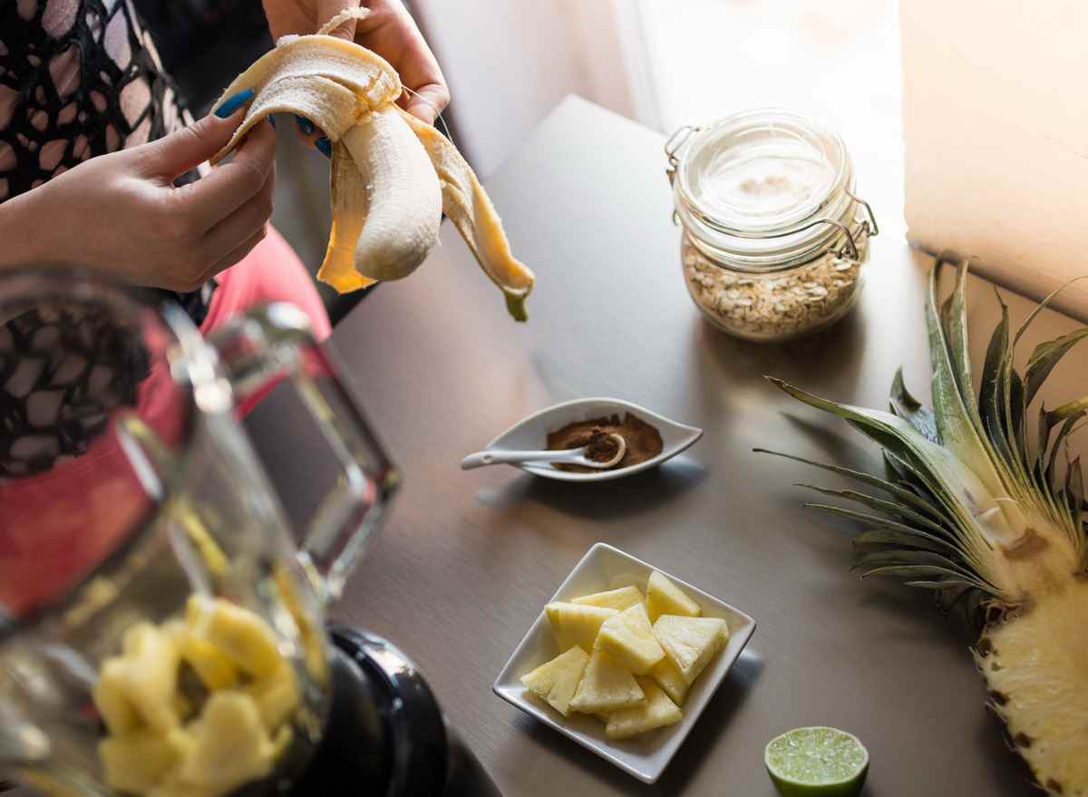 Frau schält eine Banane, um einen Ananas-Smoothie zu machen
