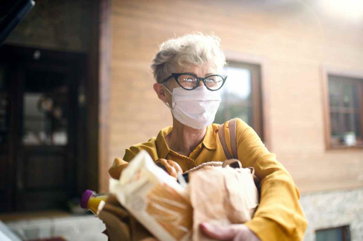 Ältere Frau mit Gesichtsmaske im Freien mit Einkaufs-, Koronavirus- und Quarantänekonzept.