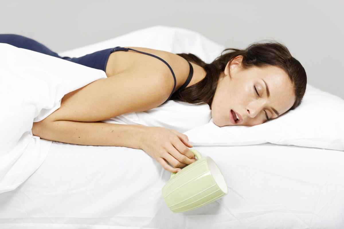 Junge Frau schläft im Bett mit Getränk in der Hand ein