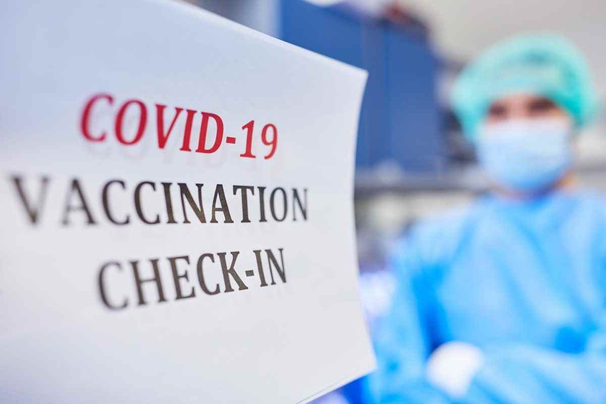 Check-in zur Coronavirus-Impfung gegen Covid-19 mit Arzt im Hintergrund.