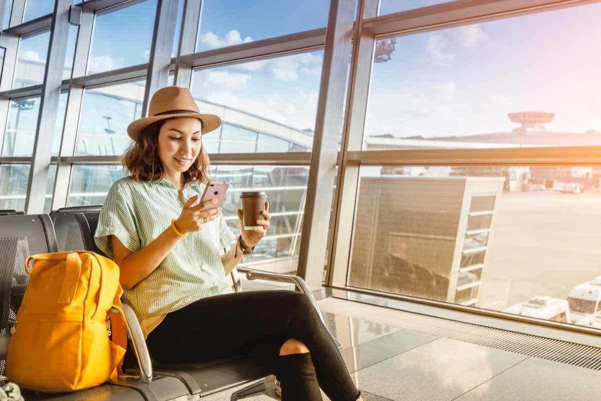 junge Frau in Fedora trinkt Kaffee am Flughafen
