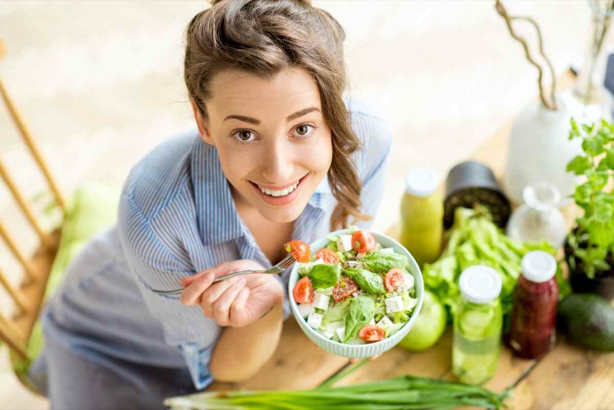 Glückliche Frau, die drinnen gesunden Salat mit grünen frischen Zutaten auf dem Tisch isst