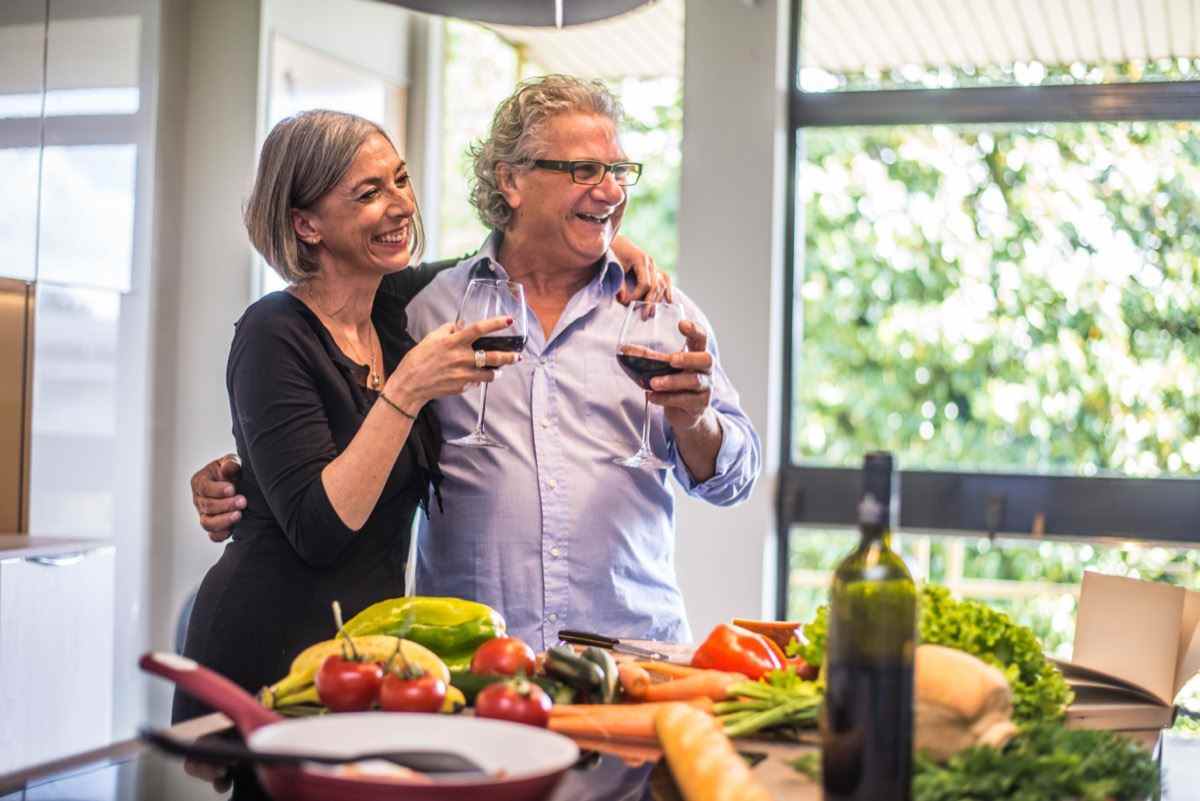 Älteres Paar, das gesundes Essen kocht und Rotwein in der Hausküche trinkt.