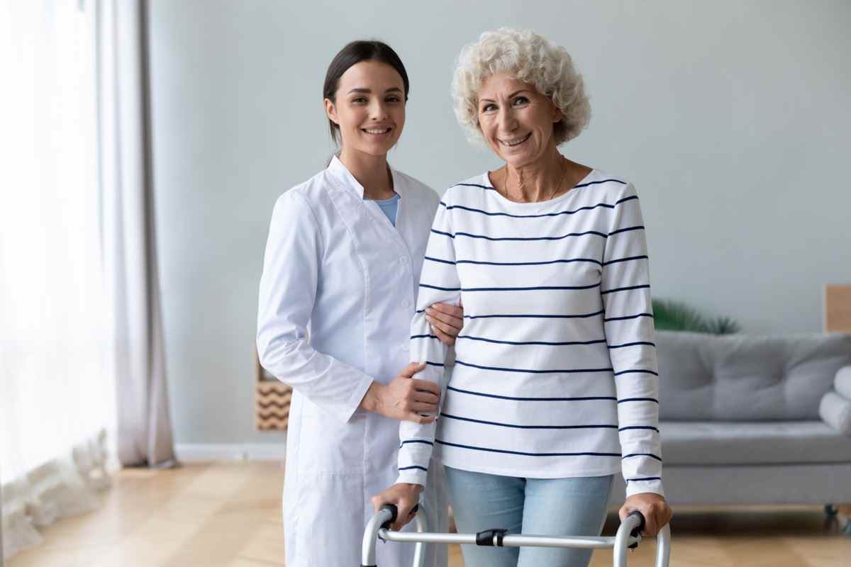 Weibliche Pfleger Physiotherapeut hilft glücklichen alten Frauenpatienten mit Gehhilfe.
