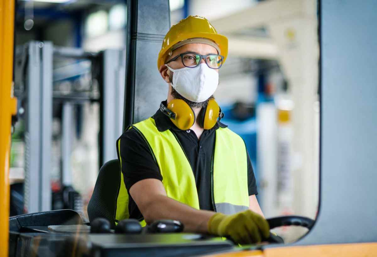 Mann Arbeiter Gabelstaplerfahrer mit Schutzmaske, die in einer Industriefabrik oder einem Lager arbeitet.