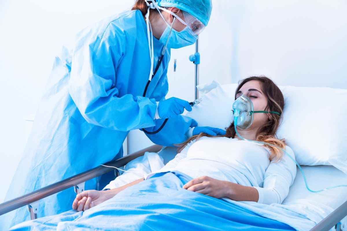 Arzt untersucht weibliche Patientin in kritischen Gesundheitszuständen mit einem Stethoskop auf der Intensivstation eines modernen Krankenhauses während der Covid-19-Pandemie