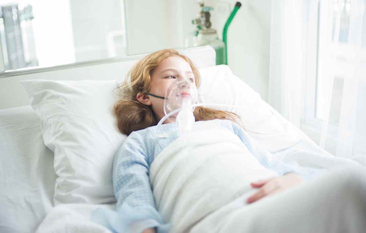 Kleines Mädchen ist krank mit Sauerstoffmaske auf ihrem Gesicht, das im Krankenhaus im Bett liegt.