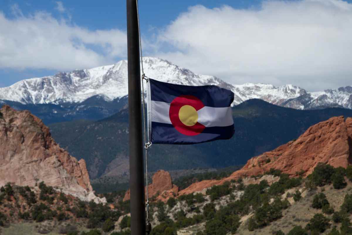 Colorado State Flag mit Pikes Peak und Garden of the Gods im Hintergrund an einem Frühlingstag
