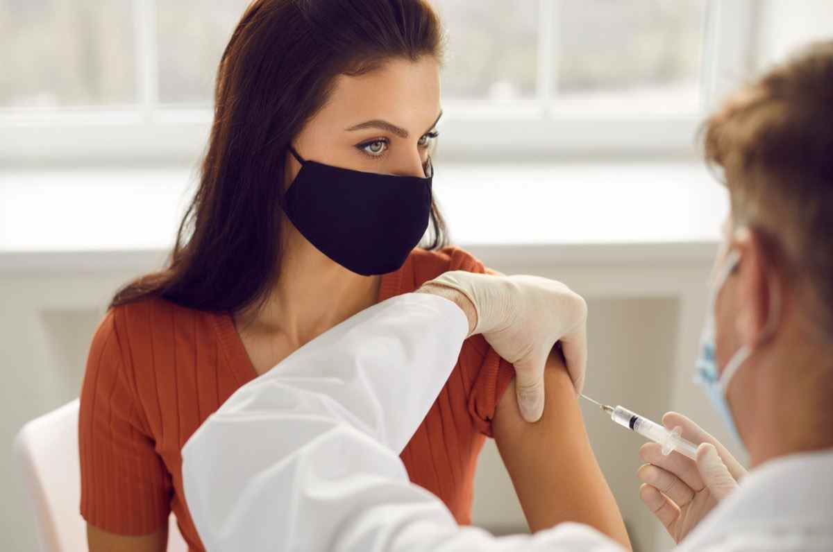 Frau in medizinischer Schutzmaske, die eine Injektion bei der Armimpfung erhält.