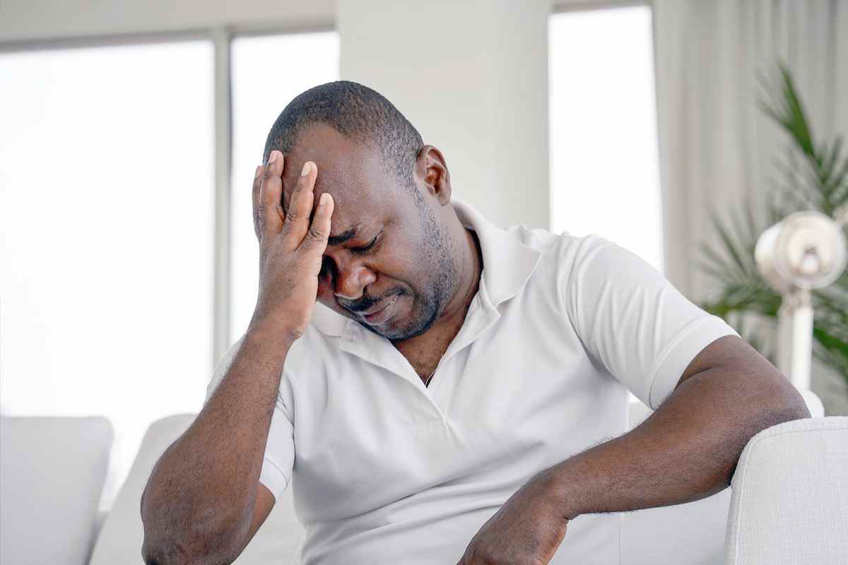 älterer Mann, der zu Hause auf dem Sofa an Kopfschmerzen leidet, Migräneschmerzen