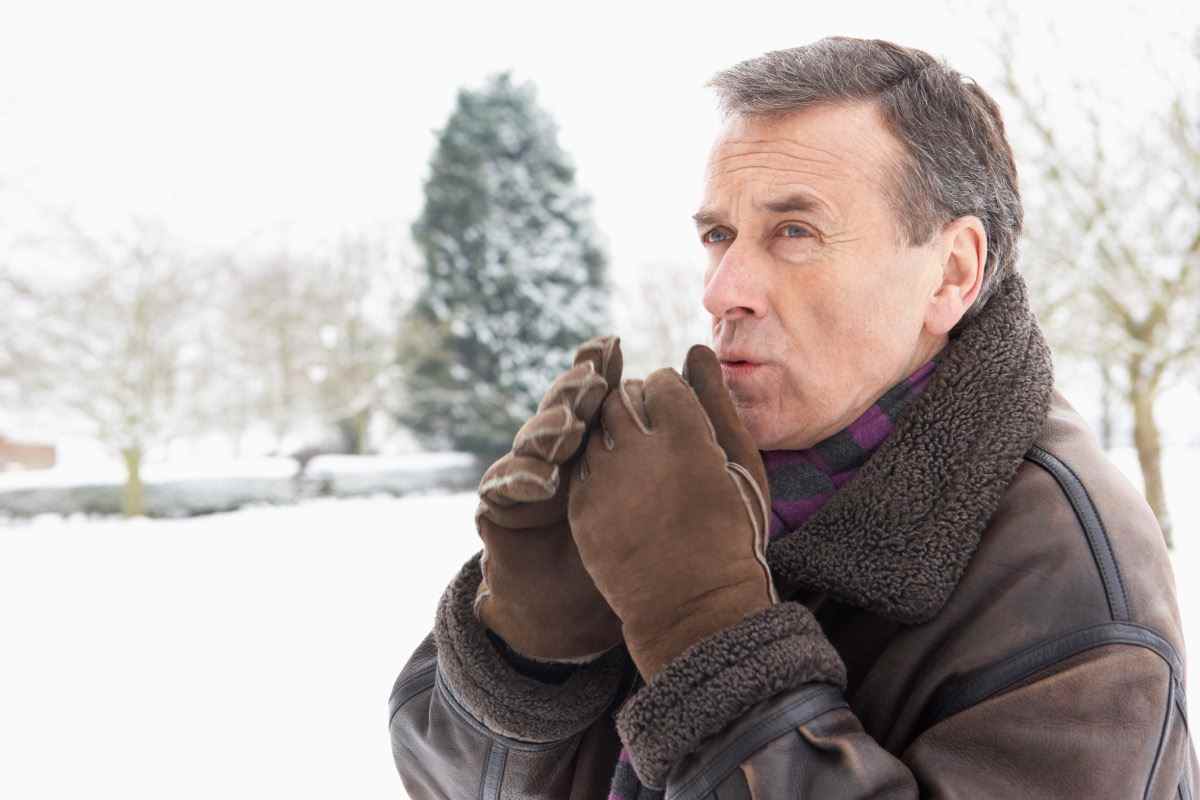 älterer Mann bläst auf behandschuhten Händen draußen im Schnee