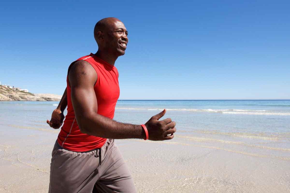 fitter Mann mittleren Alters, der an einem sonnigen Tag am Strand spazieren geht