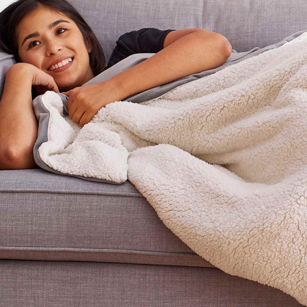Frau mit kuscheliger Helix Gewichtsdecke in weiß auf grauem Sofa