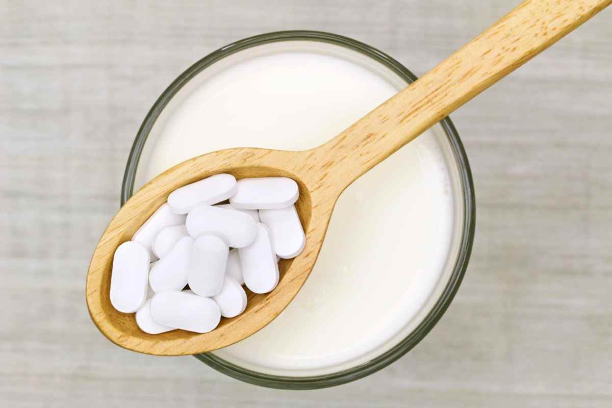 Holzlöffel Calciumcarbonat-Tabletten über einem Glas Milch