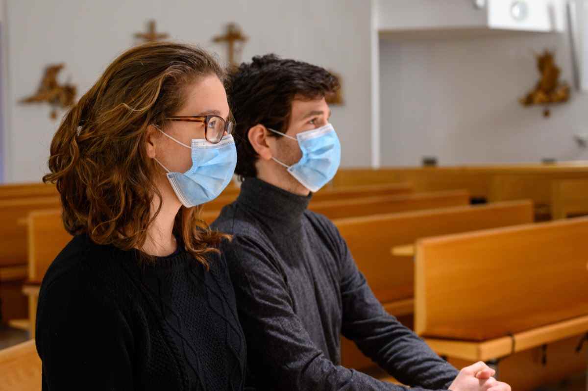 Ein junges Paar mit Gesichtsmasken, das während der COVID-19-Pandemie in einer Kirche betet.