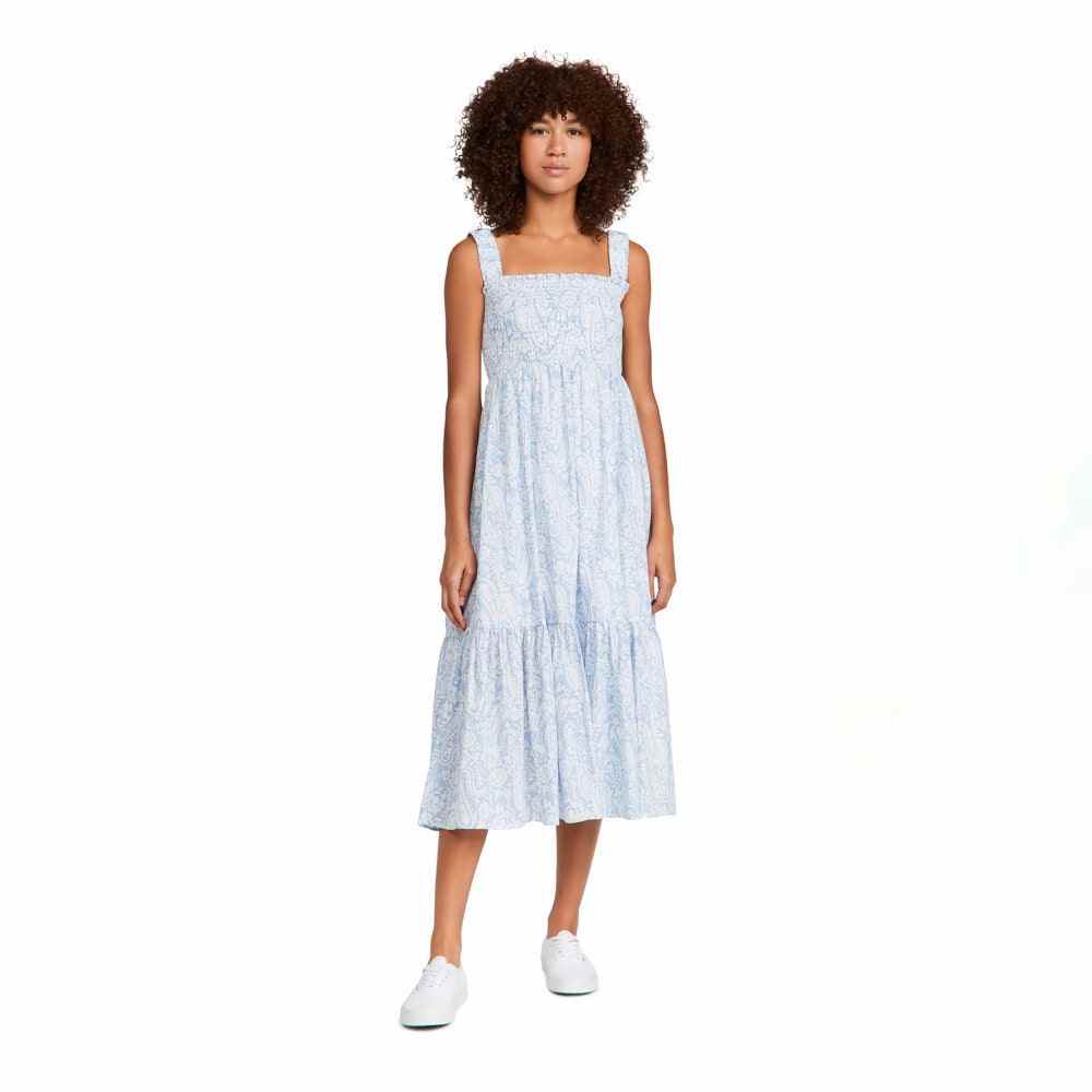 Frau trägt OPT Cotton Isla Kleid mit weißem und blauem Aufdruck und weißen Turnschuhen