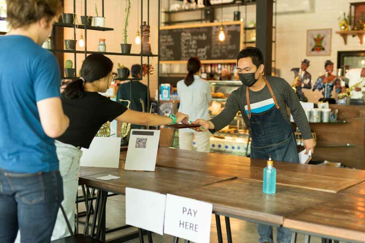 Soziale Distanz konzeptioneller Kleinunternehmen-Kellner, der Kunden im Café bedient.