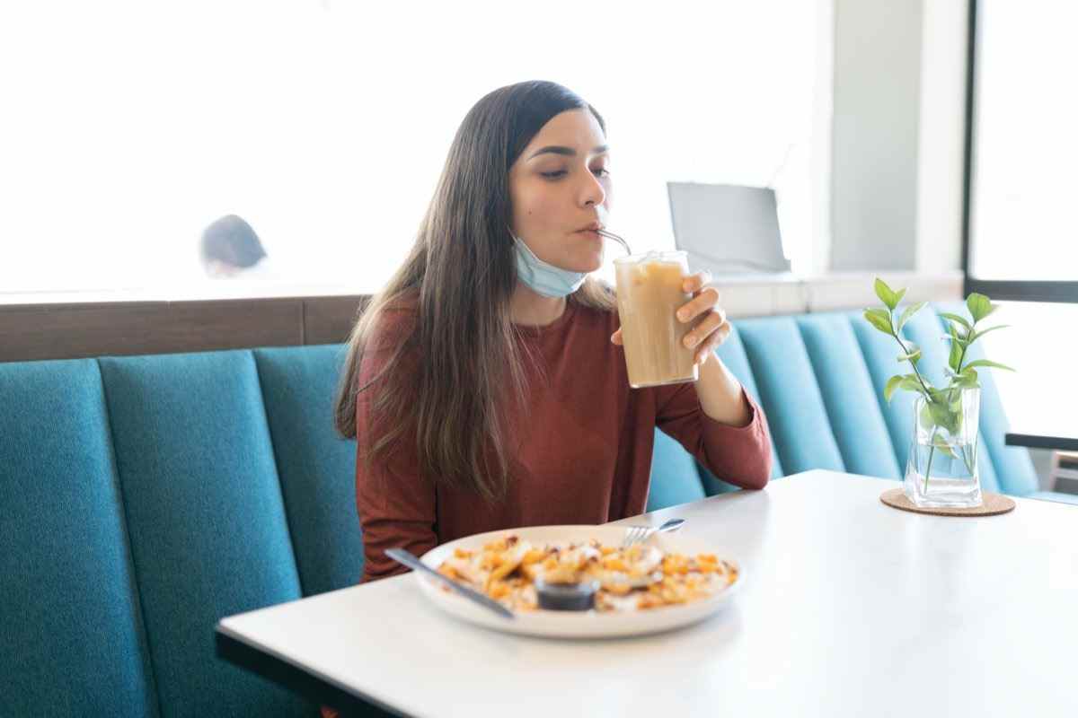 Hispanische junge Frau, die während des Ausbruchs des Coronavirus im Café trinkt