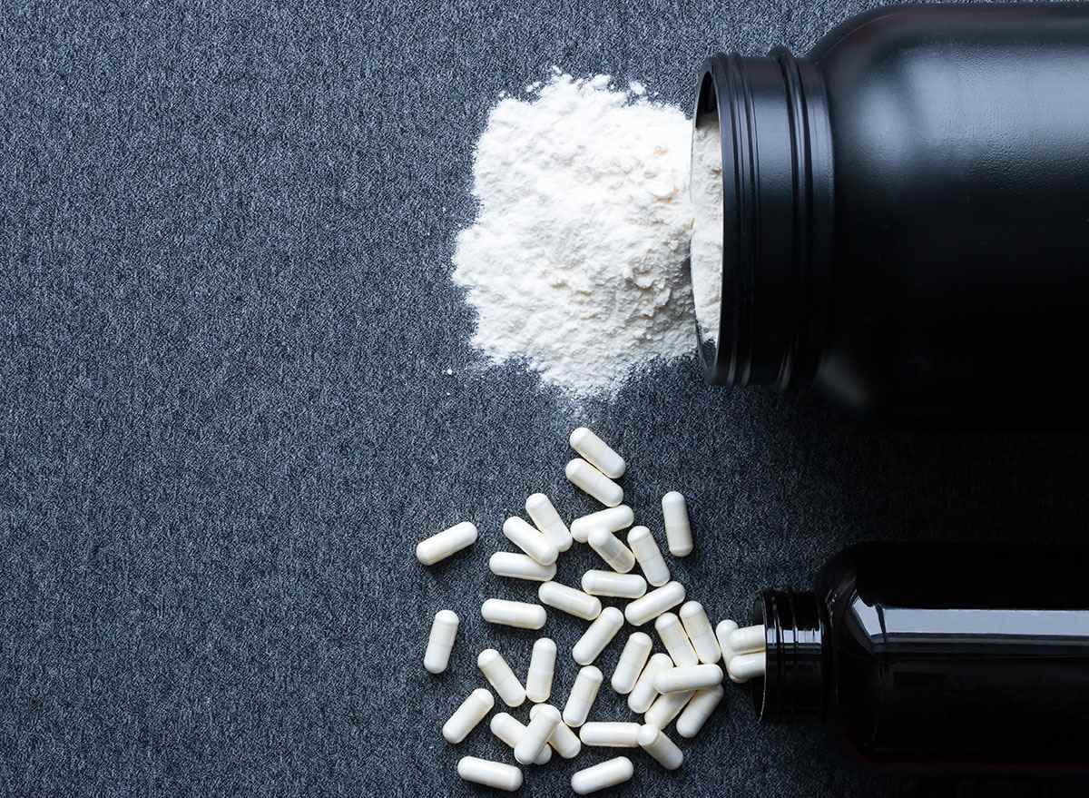 Bodybuilding-Glas Nahrungsergänzungsmittelpulver mit Pillen auf grauem Hintergrund