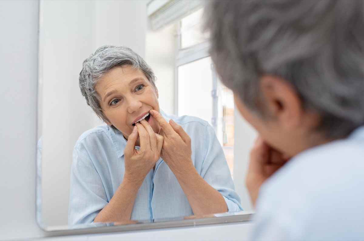 Reife schöne Frau, die ihre Zähne mit Zahnseide im Badezimmer putzt