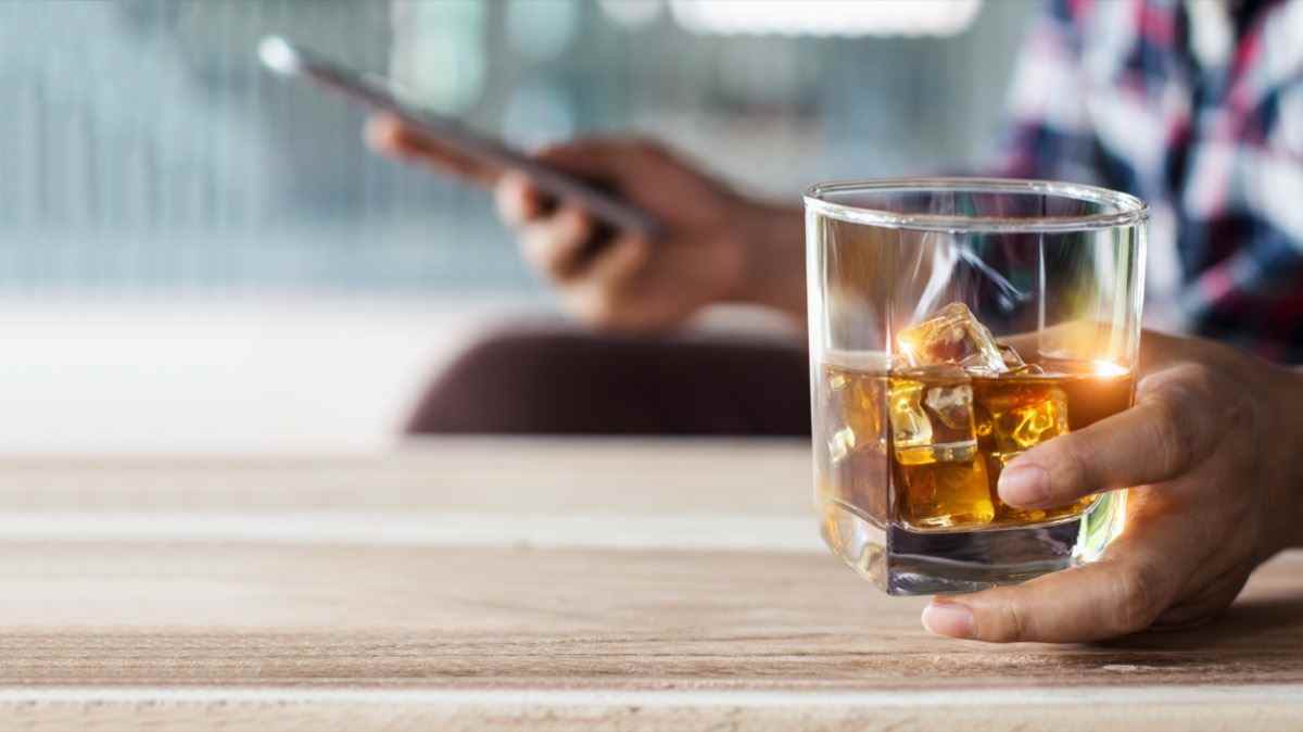 Mann, der sich mit Bourbon-Whisky-Getränk in der Hand entspannt und mobiles Smartphone verwendet