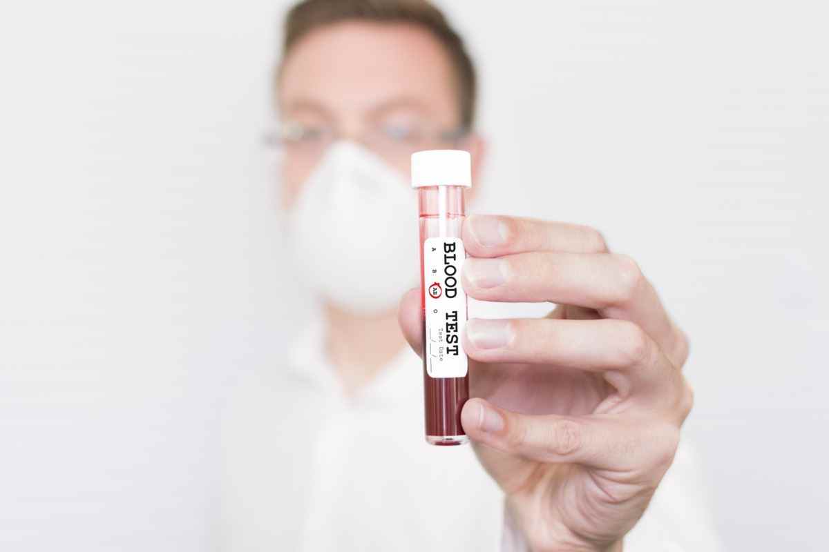 Ein männlicher Wissenschaftler/Arzt, der ein Reagenzglas mit der Aufschrift Blood Test mit der eingekreisten Gruppe AB hält.