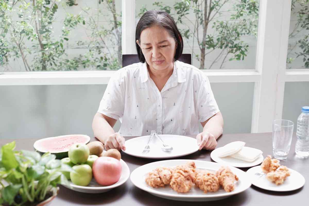 ältere Frau, die keinen Hunger hat, wenn sie Teller mit Essen betrachtet