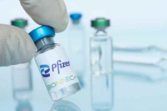 Glasflasche mit Logo Pfizer und BioNTech in der Hand des Arztes.