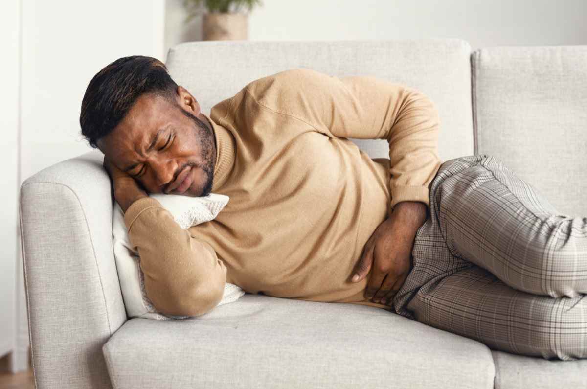Unter Bauchschmerzen leiden, die schmerzenden Magen berühren und zu Hause auf der Couch liegen