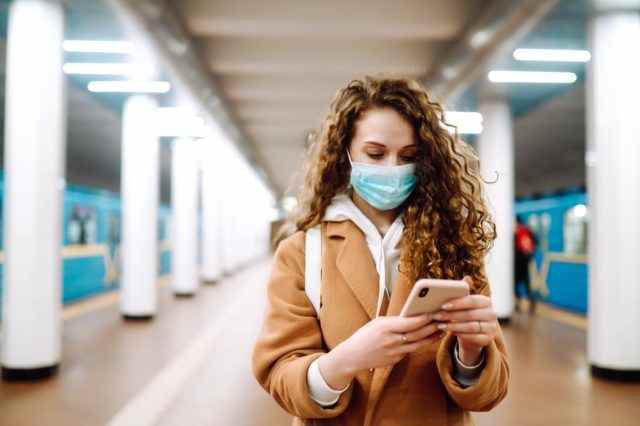 Mädchen in steriler medizinischer Schutzmaske mit einem Telefon an der U-Bahn-Station
