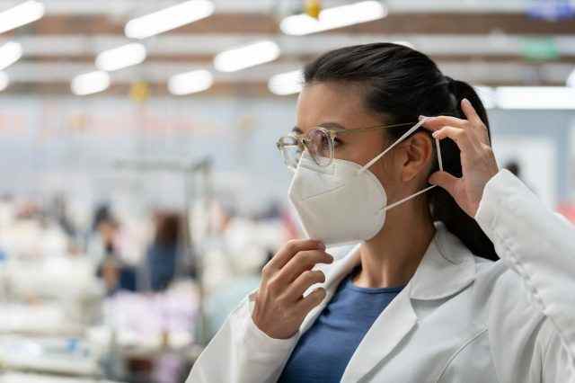 Frau, die während der COVID-19-Pandemie in einer Textilfabrik arbeitet und ihre Gesichtsmaske repariert