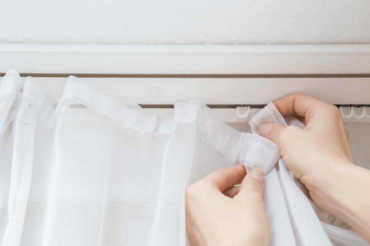 Frauenhände hängen gewaschene und saubere Tagesvorhänge am Fenster im Haus.  Kümmert sich um Hauskonzept.